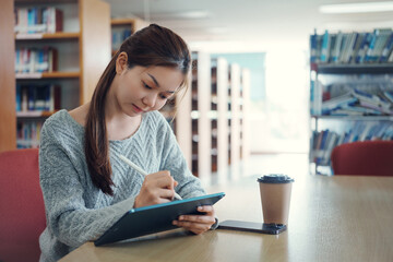 Young asian female college student using digital tablet in college library.