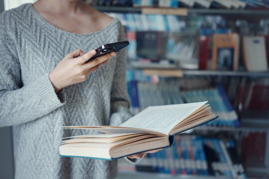Young asian female college student using a smartphone taking a photo of a book page in the school library.