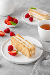 Traditional French dessert millefeuille with vanilla cream and fresh berries on a white plate on a gray concrete background.