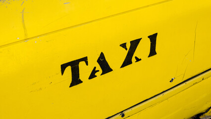 Close up of the word taxi hand painted in black lettering on the side of a yellow taxi cab in...