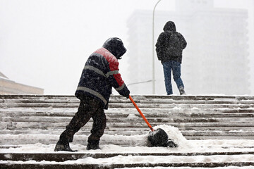 Worker cleaning street staircase with shovel, snow removal in winter city