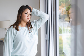 Young plus size biracial woman looks contemplative by a window at home