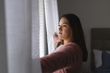Young plus size Biracial woman looks out the window thoughtfully at home