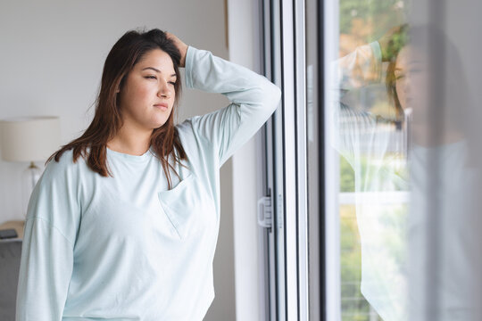 Young plus size biracial woman looks contemplative by a window at home