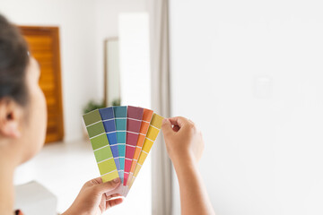 Young biracial woman compares paint samples on a wall at home
