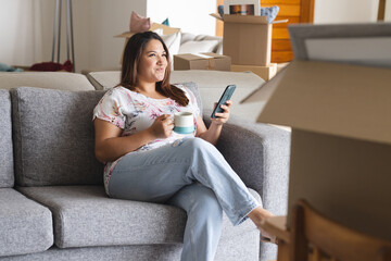 Young plus size biracial woman relaxes on a couch at home, surrounded by moving boxes, with copy spa