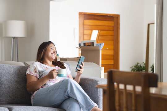 Young plus size biracial woman enjoys a video call at home, surrounded by moving boxes, with copy sp