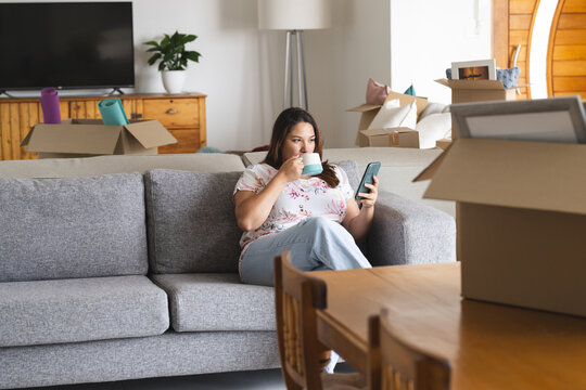 Young plus size biracial woman relaxes on a couch at home, surrounded by moving boxes