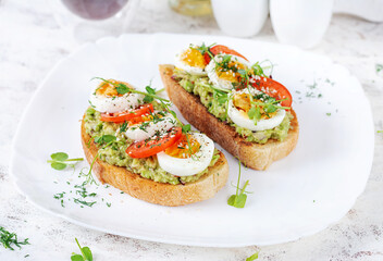 Delicious toast with avocado, boiled egg, tomatoes and microgreen on a white plate. Healthy eating, breakfast. Keto diet food. Trendy food.
