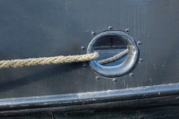 Closeup of a thick twisted mooring rope coming out of hole in the side of a metal ship.