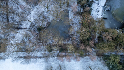 This aerial image reveals a serene winter landscape where a narrow waterway meanders through a frosted terrain. The trees, dusted with snow, create delicate patterns that weave through the ground