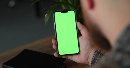 A man holding a green smartphone screen with a chromatic key is viewing content without touching or...