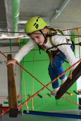 The girl carefully and cautiously passes the cableway in the playroom.
