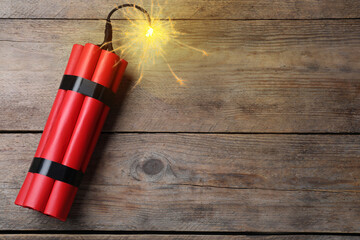 Dynamite bomb with lit fuse on wooden table, top view. Space for text