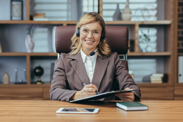 Mature professional businesswoman wearing a headset and beaming with confidence as she works from her well-appointed office.