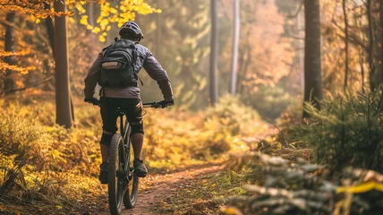 Tuinposter A cyclist with a backpack rides along a scenic forest trail amidst golden autumn foliage. © nextzimost