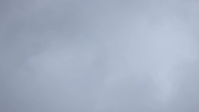 This time-lapse captures the understated elegance of an overcast sky, with fast-flowing clouds sweeping across the frame. The subtle gradients of white and gray convey a soft, diffused light, offering