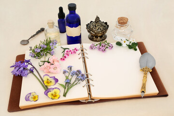 Naturopathic herbal medicine preparation with spring flowers, herbs and essential oil bottles with notebook. Alternative natural flower essences and remedies on hemp paper.