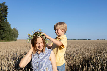 happy family, mother and son in a wheat field. The concept of parental love, motherhood. the boy puts a wreath of daisies on his mothers head. enjoy nature and life, togetherness. Earth Day