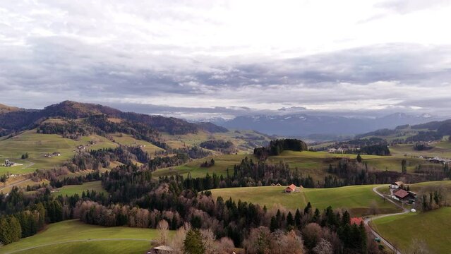 Drone flight over the hilly landscapes of the canton of Zurich on a cloudy day with mountains in the background