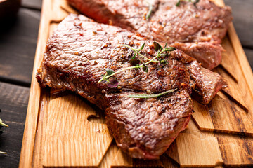 Grilled beef steak, well done with seasons and green on a black wooden background close up