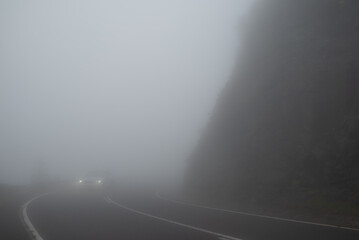 Foggy mountain curvy road and approaching car with headlights on