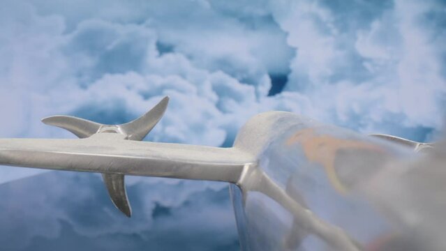 Macro lens view of silver model airplane from the back at an angle with clouds in the background and video moving in.