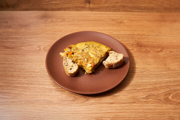 plate with a quarter of a potato omelette, sweet potato, zucchini, onion and pepper, with two pieces of bread