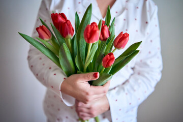 portrait of a beautiful medium-sized woman in pajamas with a bouquet of red tulips in a minimalist...