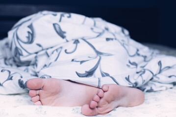 Bare feet of a child. A child in pajamas. Bare feet sticking out from under the blankets. The boy...