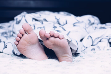 Bare feet of a child. A child in pajamas. Bare feet sticking out from under the blankets. The boy...