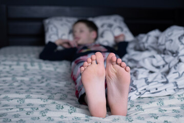 Bare feet of a child. A child in pajamas. Bare feet sticking out from under the blankets. The boy...
