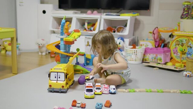 Little Girl Plays with a Toy Car. Baby Kid Play with Toys and Rolls Cars in the Parking Lot At Home Living Room. Happy Childhood Concept