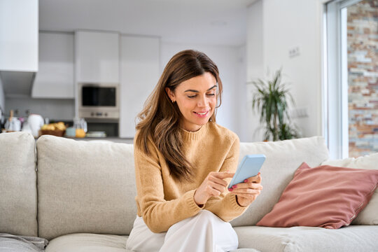 Happy mature older woman using smartphone sitting on couch at home. Smiling middle aged woman looking at cell phone messaging or doing ecommerce mobile shopping relaxing on sofa in living room.