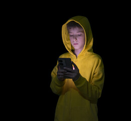 Teenager child boy wearing yellow hoodie watching videos on smart phone sitting in a dark room.