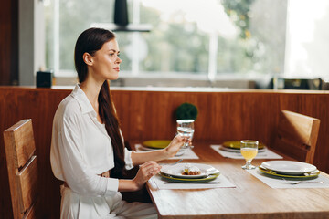 Romantic Woman Enjoying a Homemade Dinner Date at a Stylish Dining Table A beautiful brunette woman sits at an elegant dining table adorned with delicious food, including a cake and a wine glass With