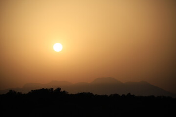 setting sun above a mountain range in hazy sahara desert dust light