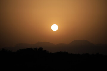 setting sun above a mountain range in hazy sahara desert dust light