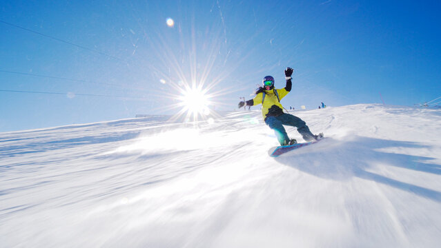 Girl snowboarding on slopes. Sun rays and flare visible.