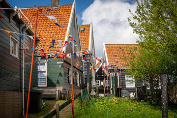 Street filled with flags in the village of Marken with traditional colorful houses in Holland Dutch island peninsula the IJsselmeer Marken on the IJsselmeer in the Netherlands. - obrazy, fototapety, plakaty