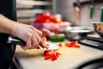 Obraz na płótnie Canvas Chefs woman hands chopping red pepper on board