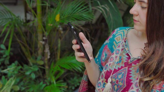 a girl in colorful clothes speaks on the phone against the backdrop of a tropical forest