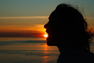 Girl silhouette with open mouth in magical sunset over the Gulf of Finland, Baltic sea.
