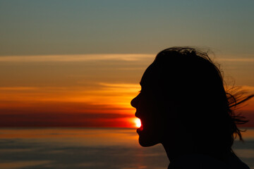 Girl silhouette with open mouth in magical sunset over the Gulf of Finland, Baltic sea.