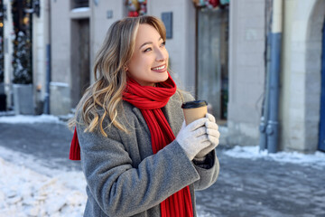 Portrait of smiling woman with paper cup of coffee on city street in winter