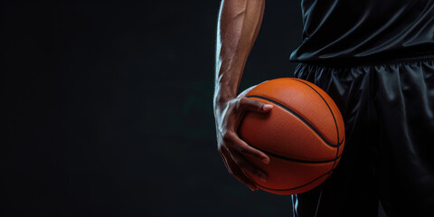 A focused athlete in a dark jersey holds a basketball against a dark background, emphasizing the readiness and determination for the game.	
