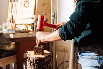 Crop of unrecognizable professional jeweler using hammer on brass doming block in workshop