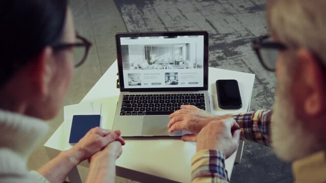 Back view image of laptop. Senior couple using laptop for online reservation, booking hotels via Internet services, choosing places. Concept of vacation, traveling, booking services