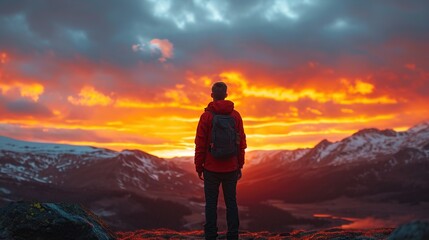 A lone figure stands before a fiery sunset backdrop, gazing at the vast mountain landscape, a vivid representation of adventure, reflection, and the grandeur of the natural world.