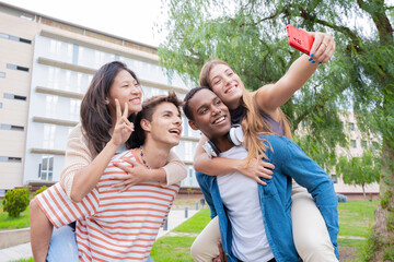  Young students piggybacking their fellow college students on campus. Excited friends posing for a funny photo.